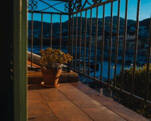 A serene view from a balcony overlooking a harbor, featuring a potted plant and warm sunset tones.