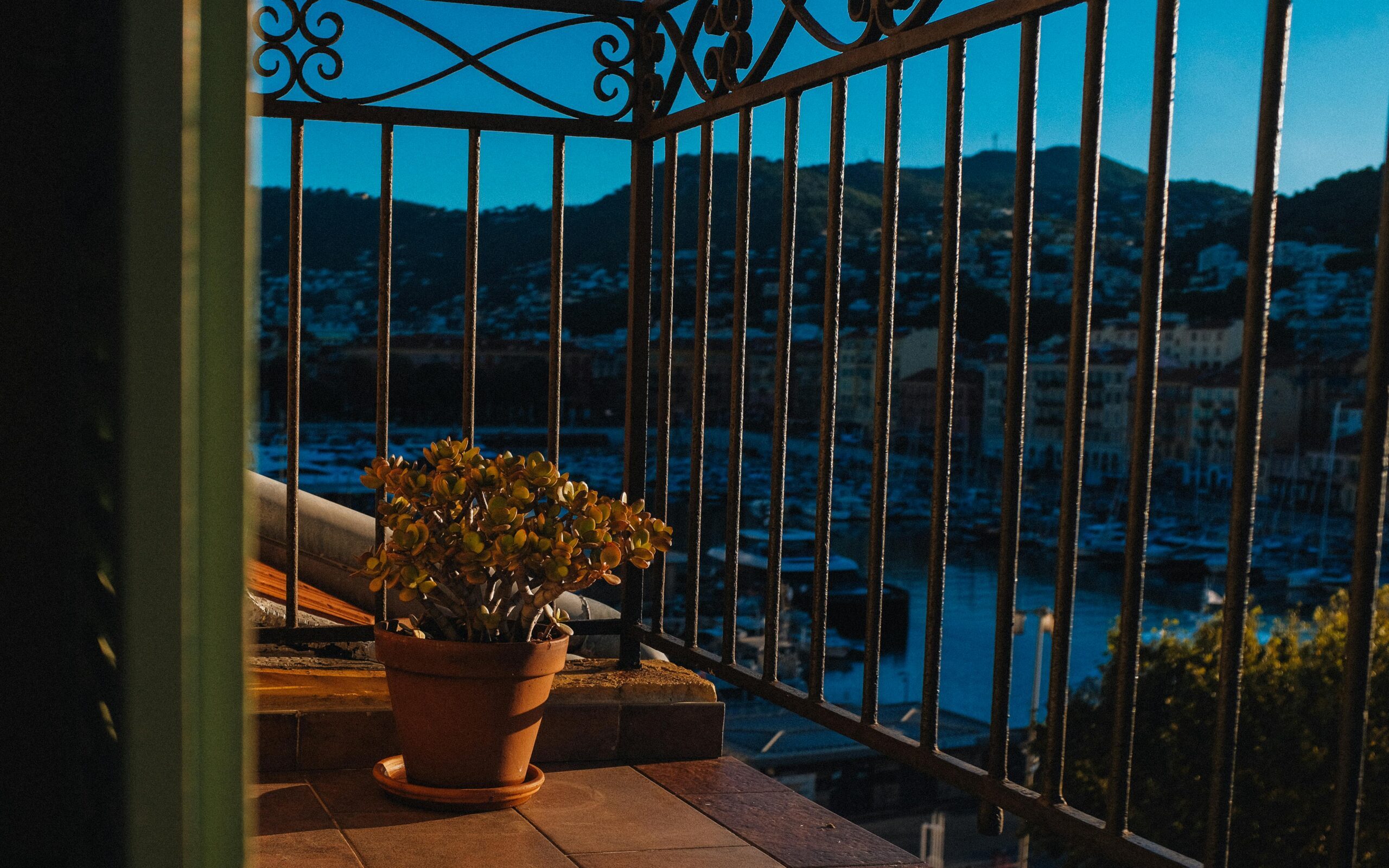 Intero Appartamento A serene view from a balcony overlooking a harbor, featuring a potted plant and warm sunset tones.