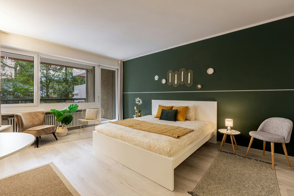 A stylish, modern bedroom with a green accent wall, contemporary decor, and ample natural light.